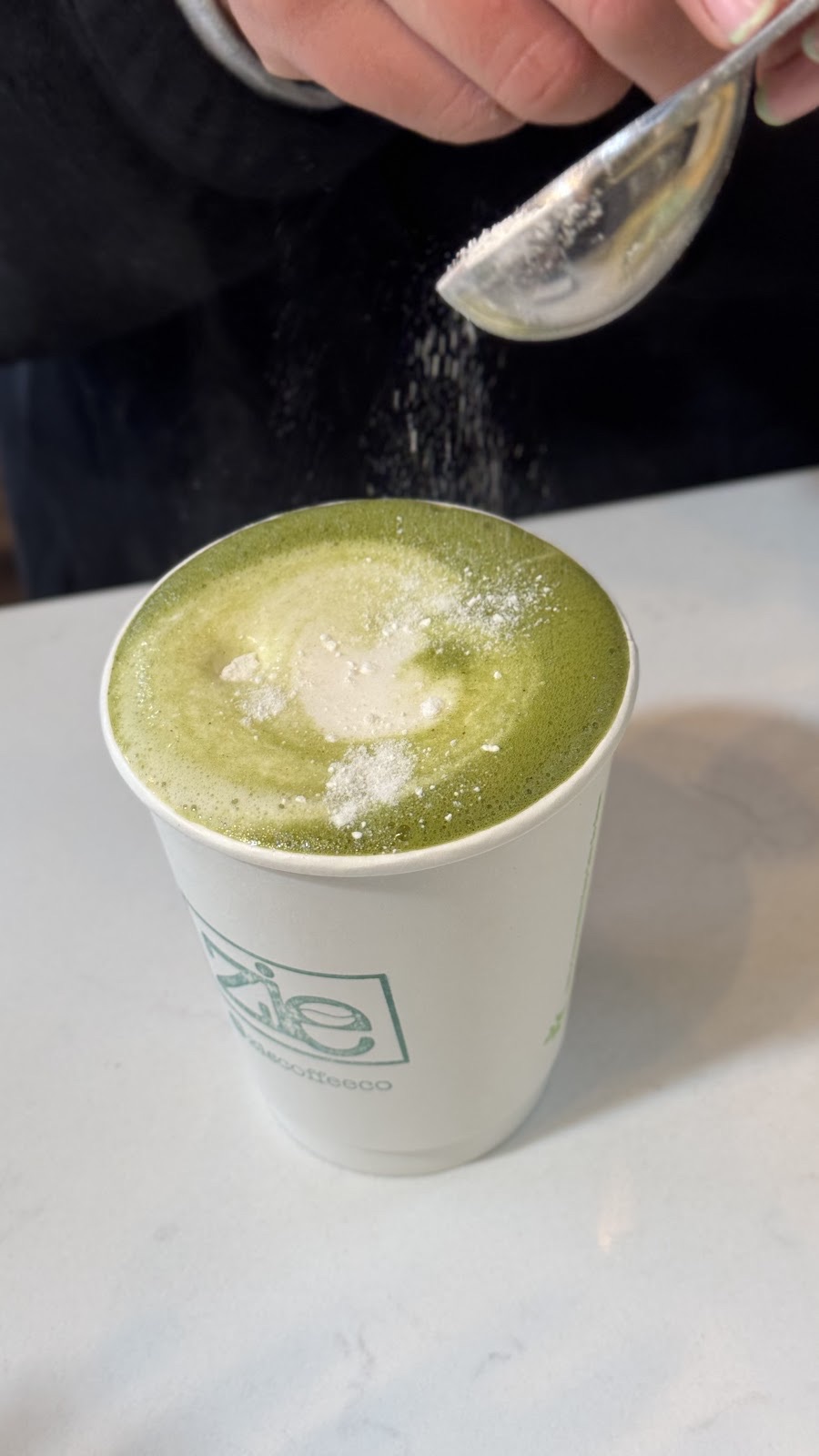 A matcha latte being dusted with powder from a spoon