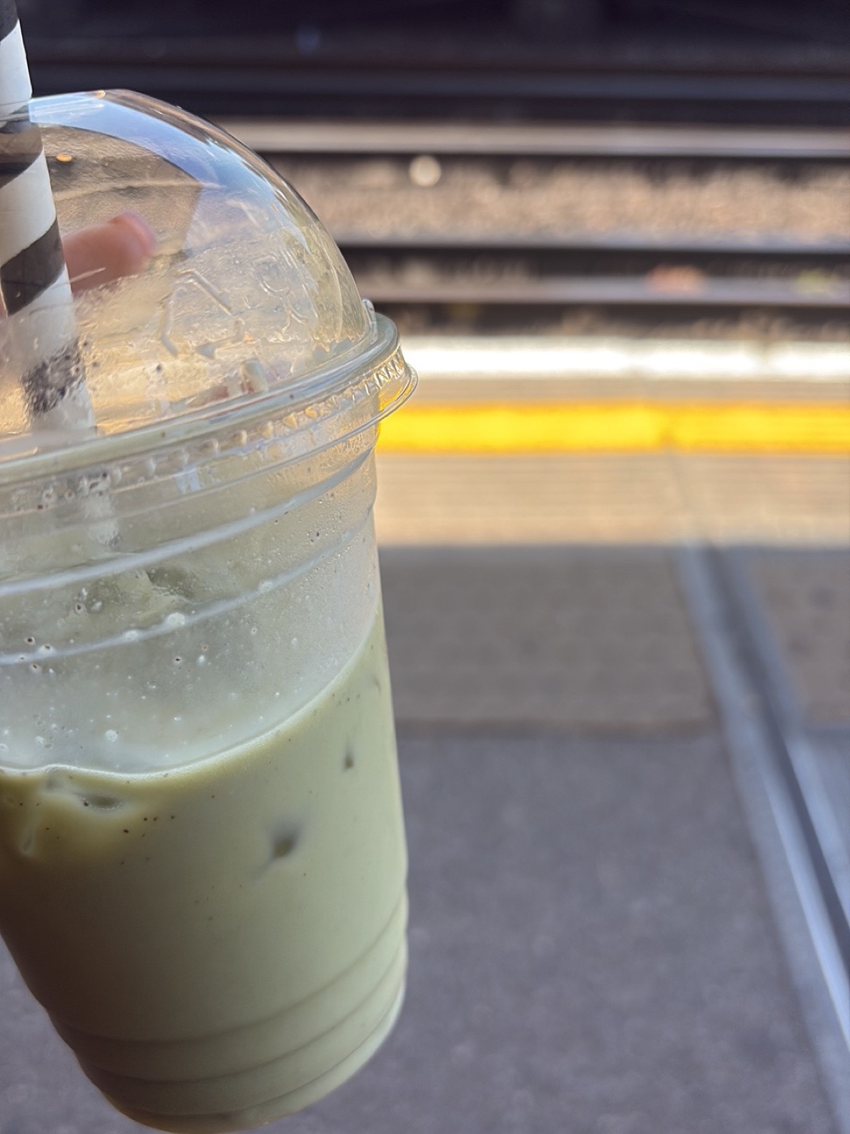 An iced matcha latte in a clear domed cup with a striped straw