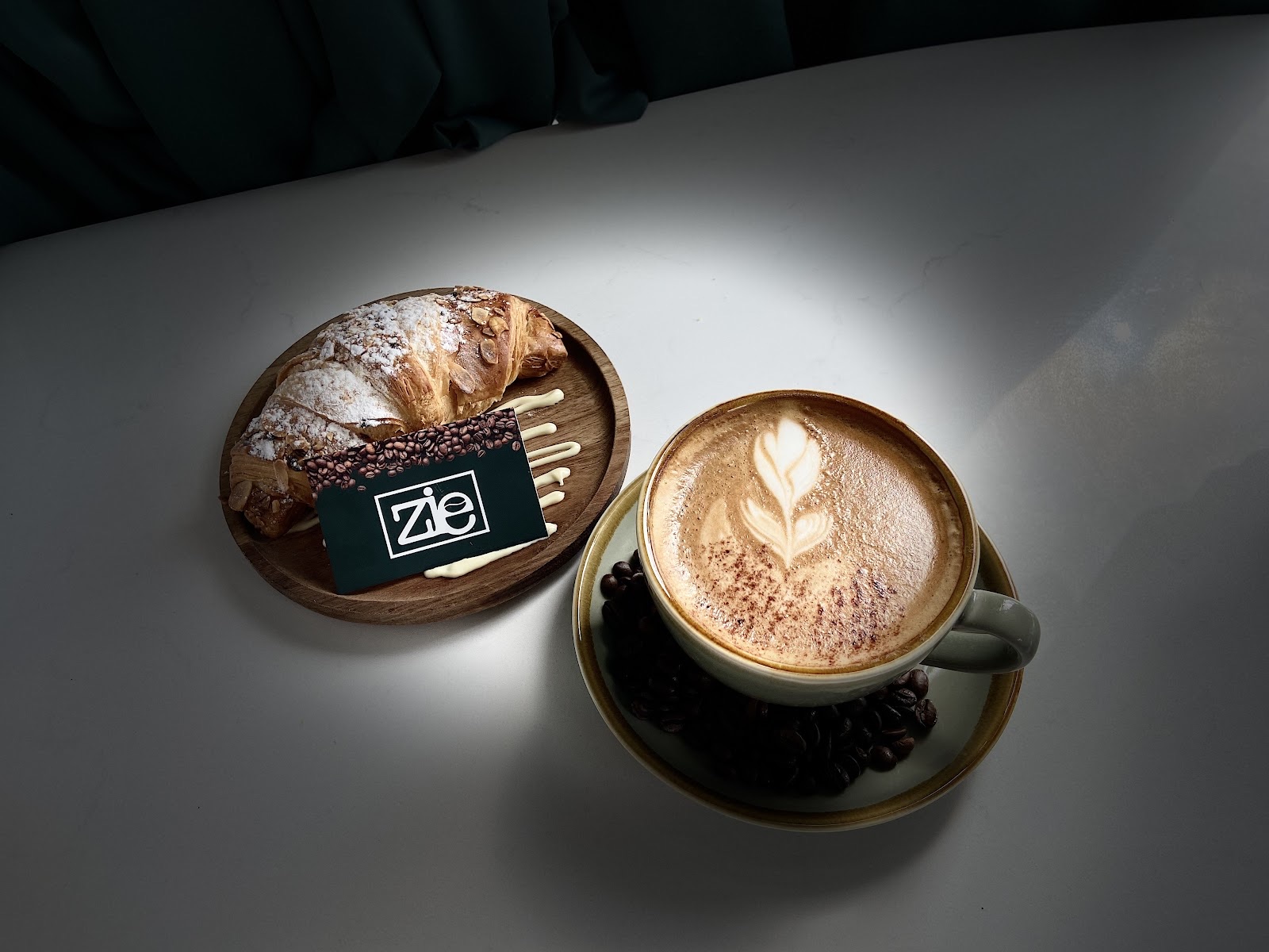 A latte with rosetta art beside a chocolate-topped pastry